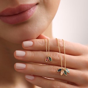 May include: Two gold necklaces with delicate leaf pendants. One necklace features a single leaf with a red and green gemstone, while the other necklace has five leaves with a variety of colorful gemstones.