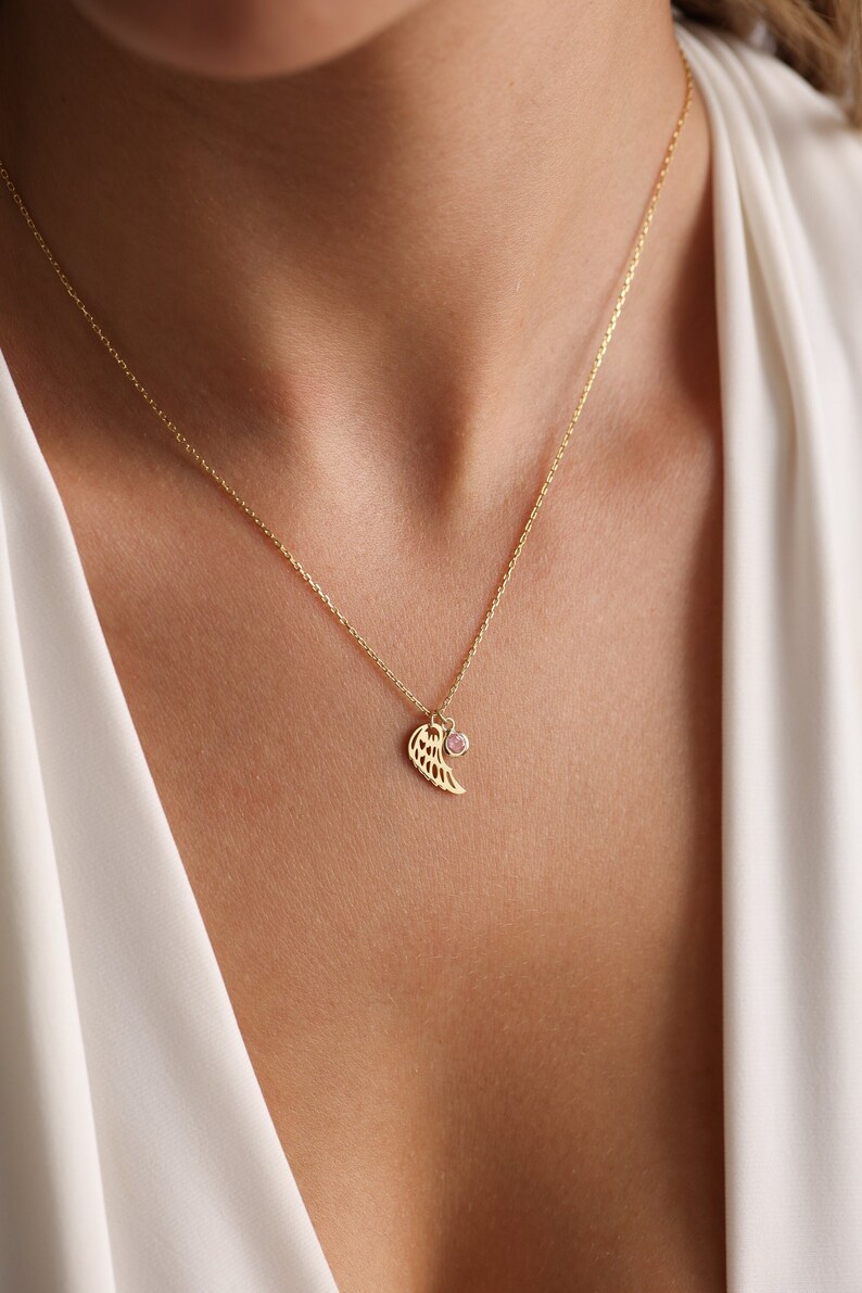 May include: A gold chain necklace with a delicate angel wing pendant and a small pink gemstone.