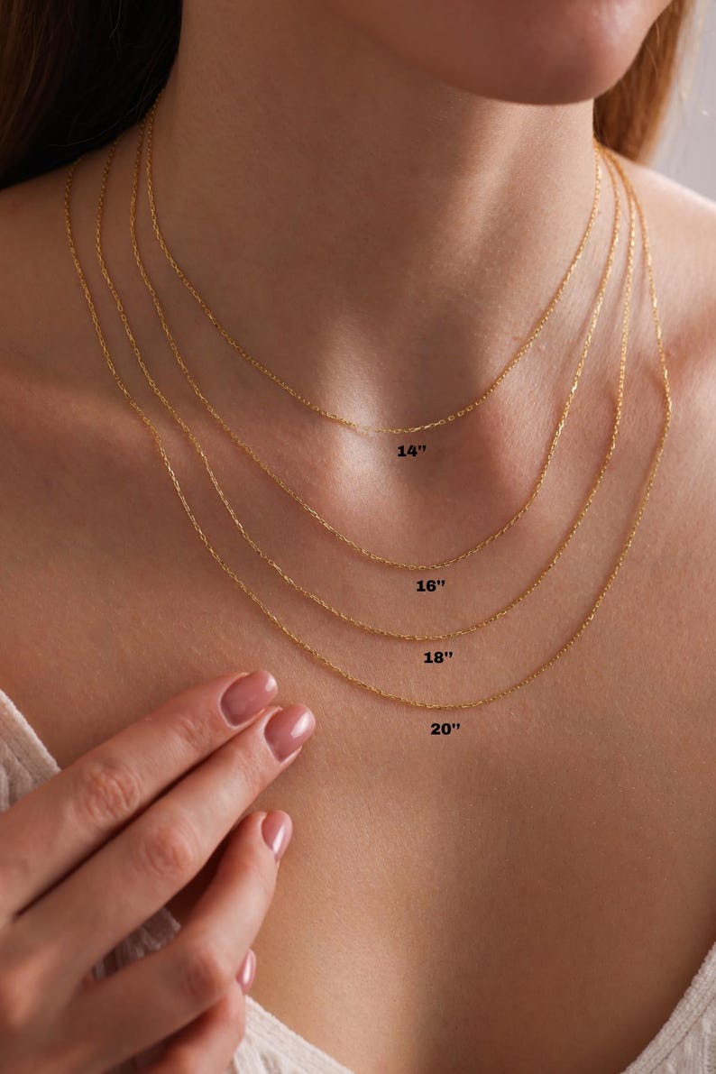 May include: Four gold chains of different lengths, 14 inches, 16 inches, 18 inches, and 20 inches, are shown on a person's neck. The chains are all the same style, with a delicate, rope-like design.
