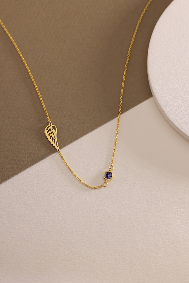 May include: A gold chain necklace with a single wing pendant and a small purple gemstone.