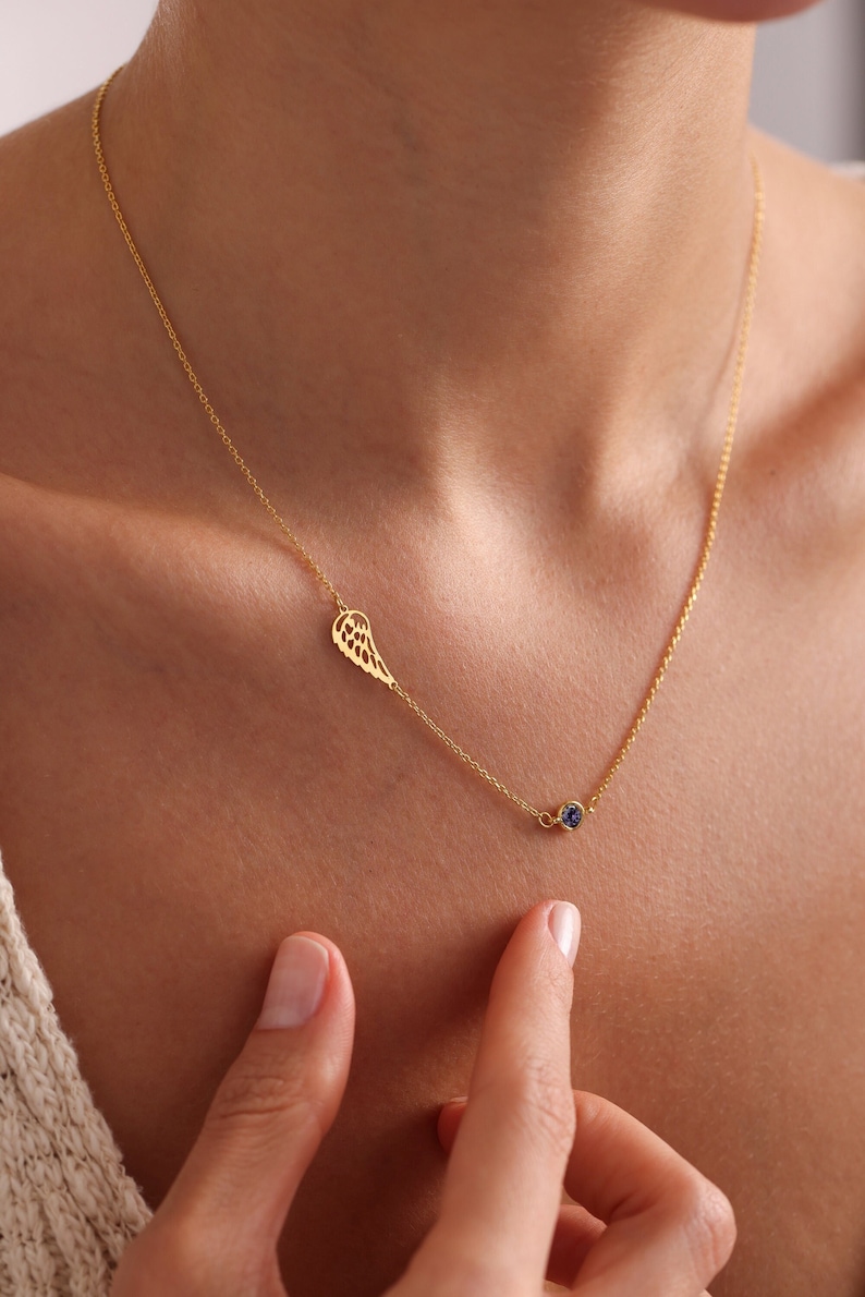 May include: A gold chain necklace with a delicate wing charm and a small blue gemstone pendant.