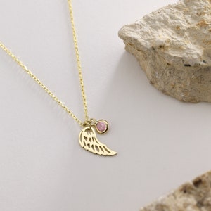 May include: A gold chain necklace with a delicate angel wing charm and a pink gemstone pendant.