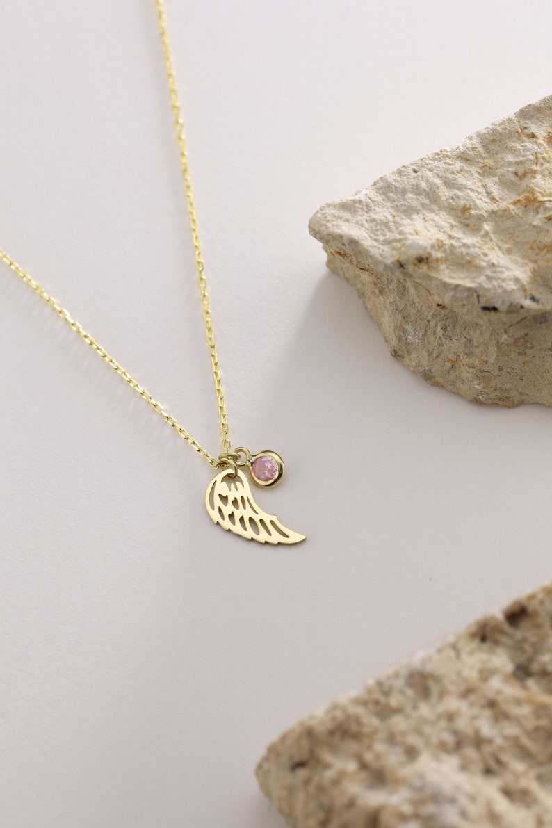 May include: A gold chain necklace with a delicate angel wing charm and a pink gemstone pendant.