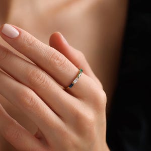 以下が含まれることがあります： エメラルドグリーン、サファイアブルー、クリアなバゲット型の宝石が並んだゴールドのバンドリングです。