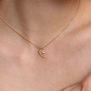 May include: A gold chain necklace with a delicate wing pendant and a small pink gemstone.