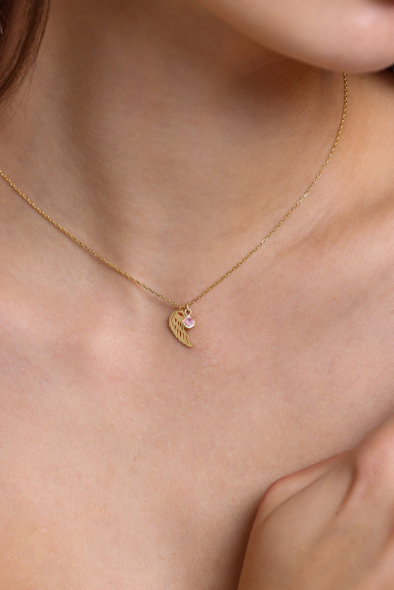 May include: A gold chain necklace with a delicate wing pendant and a small pink gemstone.