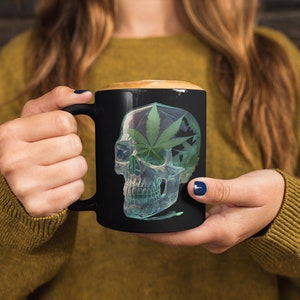 May include: Black coffee mug with a graphic of a green marijuana leaf inside a clear skull.