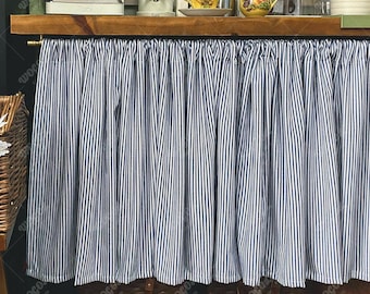May include: Blue and white striped kitchen valance. The valance is made of fabric and hangs below a wooden shelf. The stripes are vertical and evenly spaced. The valance is gathered at the top, creating soft folds.