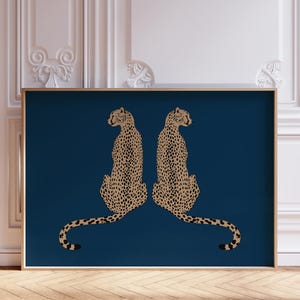 May include: A framed art print featuring two cheetahs facing each other. The cheetahs are depicted in a tan color with black spots, set against a deep blue background. The frame is a light gold color.