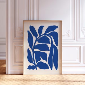 May include: A framed art print with a botanical design. The artwork displays stylized blue leaves on a cream background. The print is in a thin, light brown wooden frame, suitable for home decor.