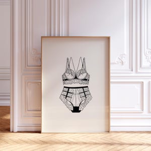 May include: Black and white line art illustration of a lingerie set. The set includes a bra with delicate lace detailing and matching high-waisted briefs. The artwork is framed in a wooden frame and displayed against a white wall.