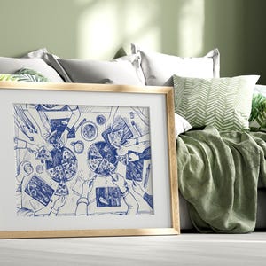 Puede incluir: Una impresión artística enmarcada representa una reunión alrededor de una mesa con pizza. La ilustración es en tinta azul sobre fondo blanco, mostrando manos que alcanzan porciones. El marco es de madera clara, y la obra se exhibe en una cama con almohadas y una manta verde.
