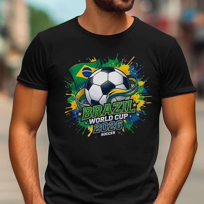 K&ouml;nnte beinhalten: Schwarzes T-Shirt mit einem Fu&szlig;ball-Design, der brasilianischen Flagge und dem Text "BRAZIL WORLD CUP 2026 SOCCER". Das Design beinhaltet gelbe, gr&uuml;ne und blaue Farbspritzer.