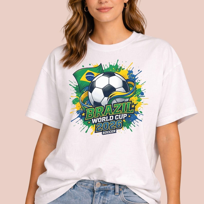 May include: White t-shirt featuring a soccer ball graphic with the text "BRAZIL WORLD CUP 2026 SOCCER". The design includes the Brazilian flag and colorful paint splatters in green, yellow, and blue.