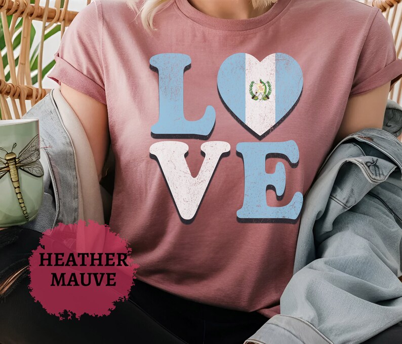 May include: Mauve t-shirt featuring the word "LOVE" in a distressed font. The "O" is a heart with the Guatemalan flag design. The shirt has short sleeves and is made of a soft material. The text "Heather Mauve" is at the bottom.