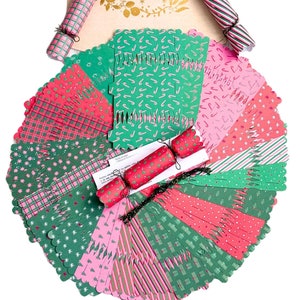 Op de afbeelding: Een set van 24 kerstcracker-kits met verschillende feestelijke patronen in roze, groen en rood. De crackers zijn versierd met snoepstokken, sterren, ruitjes en strepen. De kits bevatten een trekkoord en een klein cadeau. De tekst op de zak is "La Magie de Noël".