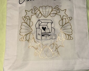 May include: White canvas tote bag with black text that says "Ostsee Liebe" and a gold design of seashells and a beach chair with a heart on it.