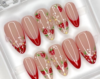 May include: Set of ten false nails with a white and red strawberry and daisy design. The nails are a light pink color with a white tip and a red accent.