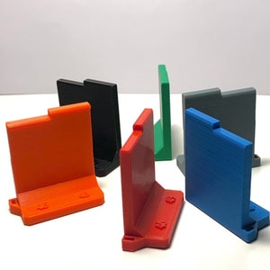 May include: Six 3D printed corner brackets in different colours: orange, red, black, green, grey, and blue. The brackets are designed to be used as corner supports for shelves or other structures.