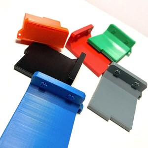 May include: Six 3D printed plastic corner pieces in different colours: orange, black, red, green, grey, and blue. Each piece has a small raised number "6" on it.