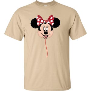 K&ouml;nnte beinhalten: Beiges T-Shirt mit Minnie Mouse-Design. Das Design zeigt Minnie's Gesicht, schwarze Ohren und eine rote Schleife mit wei&szlig;en Punkten. Eine d&uuml;nne rote Linie erstreckt sich vom Gesicht und erzeugt einen Ballon-Effekt.