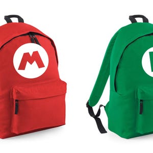 Puede incluir: Dos mochilas, una roja y otra verde. La mochila roja tiene una "M" blanca en un círculo, la verde una "L" blanca. Ambas tienen cremalleras y correas negras. Ideales para la escuela.