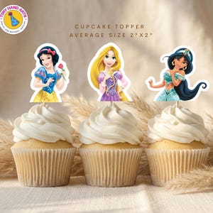 Peut inclure: Trois cupcakes ornés de décorations de gâteaux sur le thème des princesses. Les décorations représentent Blanche-Neige, Raiponce et Jasmine. Les cupcakes sont recouverts de glaçage blanc et sont dans des caissettes beiges. Le texte dit "Cupcake Topper Average Size 5cm x 5cm".