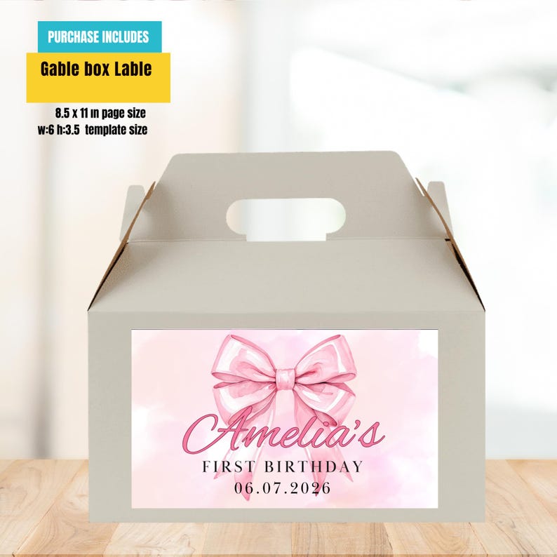 Puede incluir: Una caja gable gris claro con un dise&ntilde;o de lazo rosa y el texto "Amelia's FIRST BIRTHDAY 06.07.2026". La caja incluye un asa y una etiqueta que dice "Gable box Lable". El tama&ntilde;o de la plantilla es de 15,24 cm de ancho y 8,89 cm de alto.
