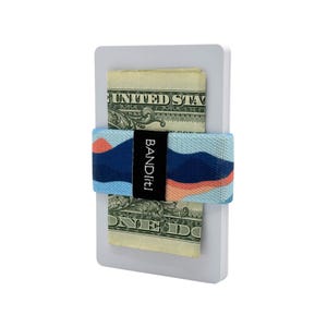 May include: A white card holder with two one-dollar bills secured by a blue, orange, and black elastic band. The band has the text "BANDit!" printed on it.