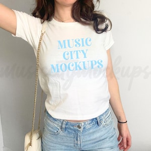 Könnte beinhalten: Ein weißes T-Shirt mit dem Text "MUSIC CITY MOCKUPS" in hellblauer Schrift.