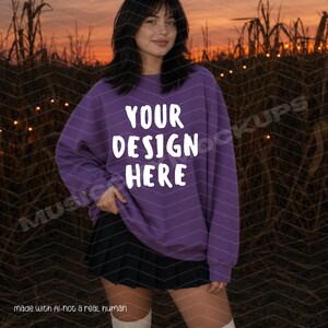 Op de afbeelding: Een paars sweatshirt met lange mouwen en de witte tekst YOUR DESIGN HERE op de voorzijde. Het kledingstuk heeft een ronde hals en geribbelde boorden, gecombineerd met een zwarte geplooide rok. Het ontwerp is eenvoudig en functioneel.