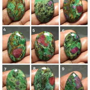 May include: A collection of nine oval-shaped gemstones, each displaying a unique pattern of green, brown, and red hues. The stones vary in the distribution of colors, with some featuring more prominent red patches. The gemstones are polished and have a glossy finish.