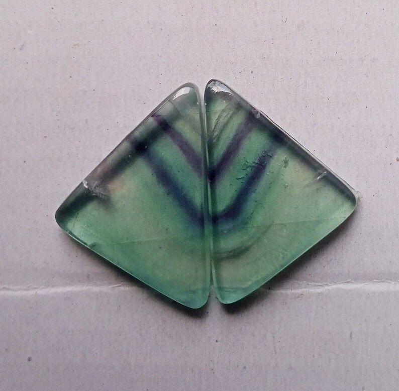Puede incluir: Dos piezas triangulares de fluorita verde con vetas p&uacute;rpuras y blancas. La fluorita es transl&uacute;cida y tiene un brillo v&iacute;treo.