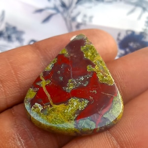 Puede incluir: Un caboch&oacute;n de jaspe rojo, verde y marr&oacute;n en forma de l&aacute;grima. La piedra tiene un patr&oacute;n de colores en espiral y est&aacute; pulida a un acabado liso.