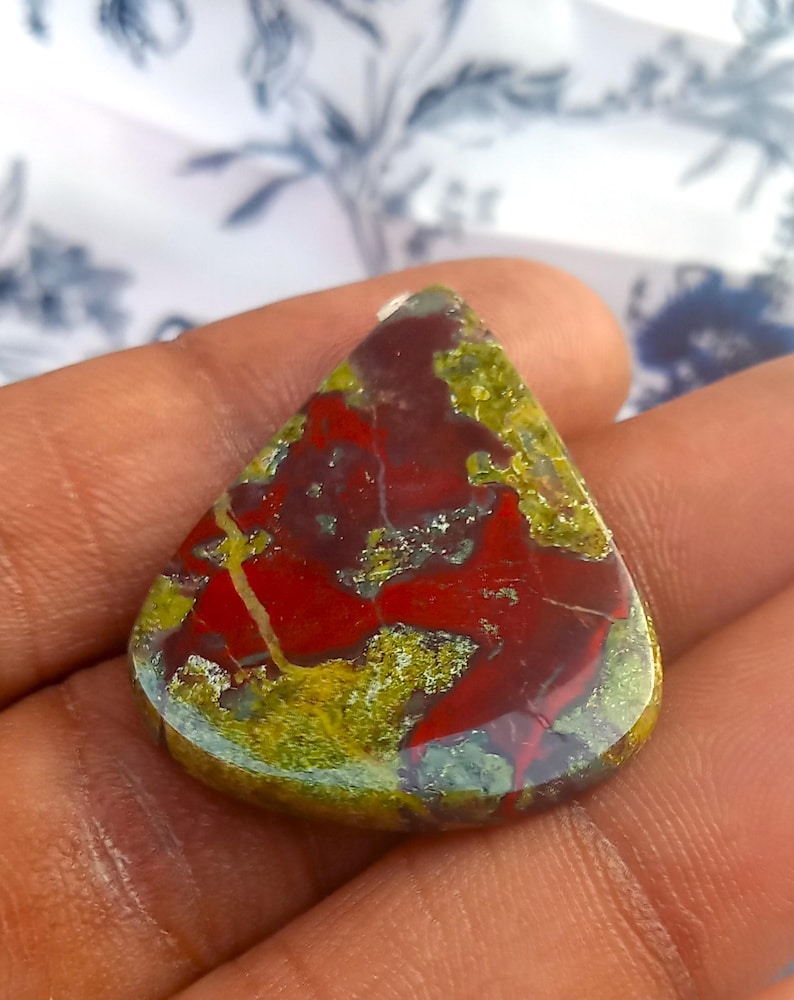 Puede incluir: Un caboch&oacute;n de jaspe rojo, verde y marr&oacute;n en forma de l&aacute;grima. La piedra tiene un patr&oacute;n de colores en espiral y est&aacute; pulida a un acabado liso.