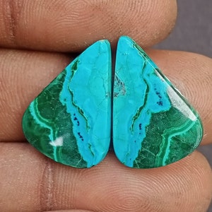 May include: A pair of turquoise and green gemstone cabochons, cut in a teardrop shape. The stones have a marbled pattern and a glossy finish.