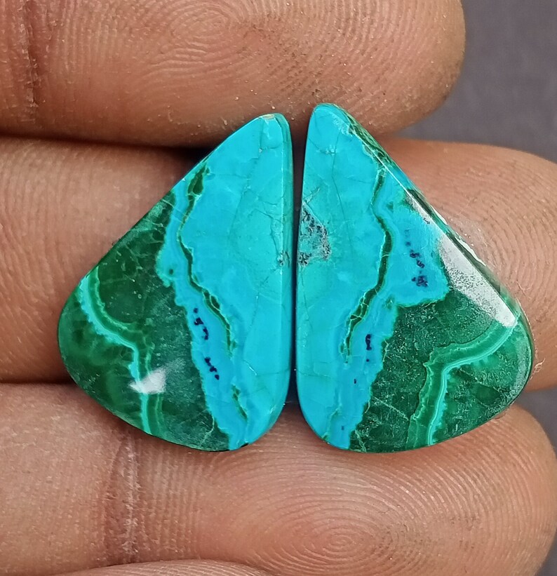 May include: A pair of turquoise and green gemstone cabochons, cut in a teardrop shape. The stones have a marbled pattern and a glossy finish.