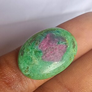 Può includere: Pietra preziosa ovale, prevalentemente verde con un'area centrale rosa intenso. La superficie della pietra ha un aspetto strutturato, con variazioni di colore. Probabilmente è un tipo di minerale.