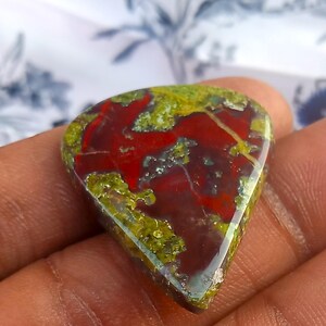 Puede incluir: Un cabuj&oacute;n de piedra preciosa roja, verde y marr&oacute;n con un patr&oacute;n &uacute;nico y arremolinado. La piedra preciosa tiene forma de l&aacute;grima y una superficie lisa y pulida.