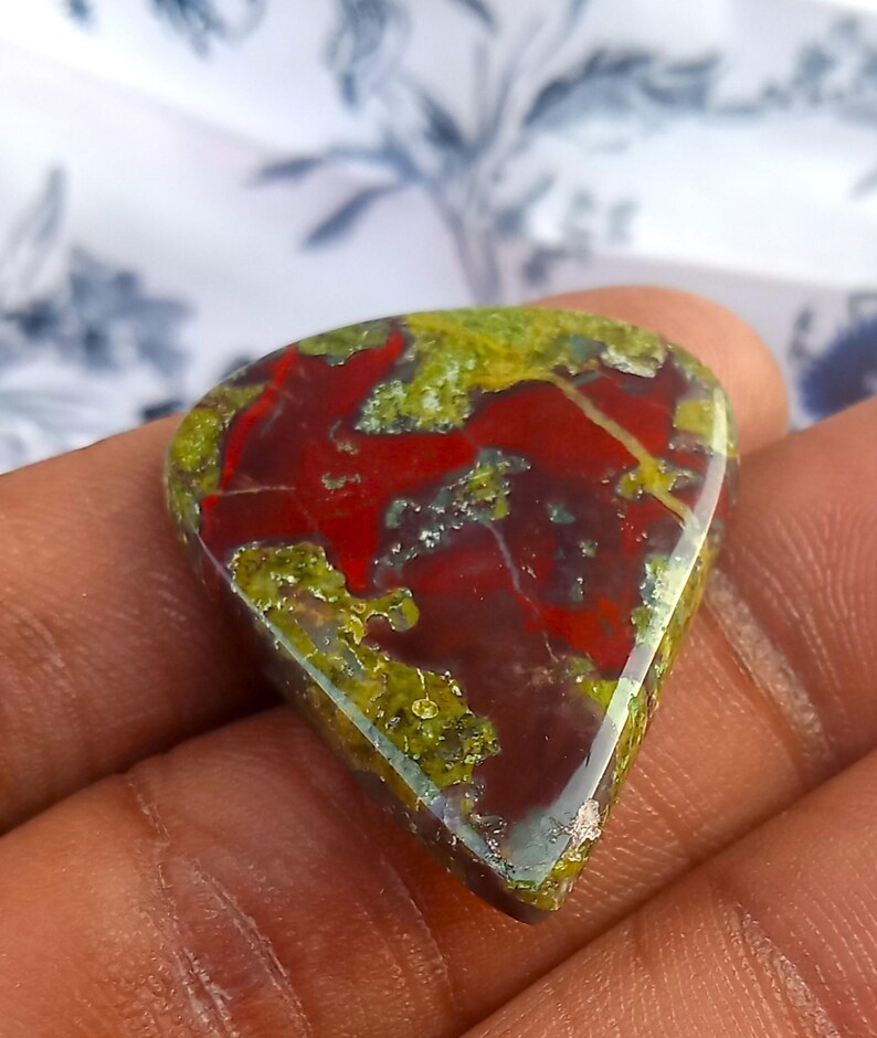 Puede incluir: Un cabuj&oacute;n de piedra preciosa roja, verde y marr&oacute;n con un patr&oacute;n &uacute;nico y arremolinado. La piedra preciosa tiene forma de l&aacute;grima y una superficie lisa y pulida.