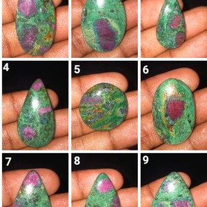 Può includere: Nove cabochon di zoisite rubino verde e rosa di varie forme e dimensioni. I cabochon sono esposti su una mano.