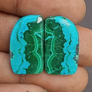 May include: Two green and blue gemstone cabochons with a marbled pattern. The cabochons are cut in a rounded rectangle shape.