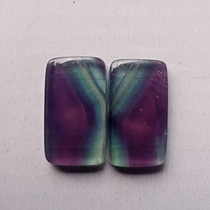 Puede incluir: Dos piedras preciosas de fluorita rectangulares con un patr&oacute;n de color morado, verde y blanco.