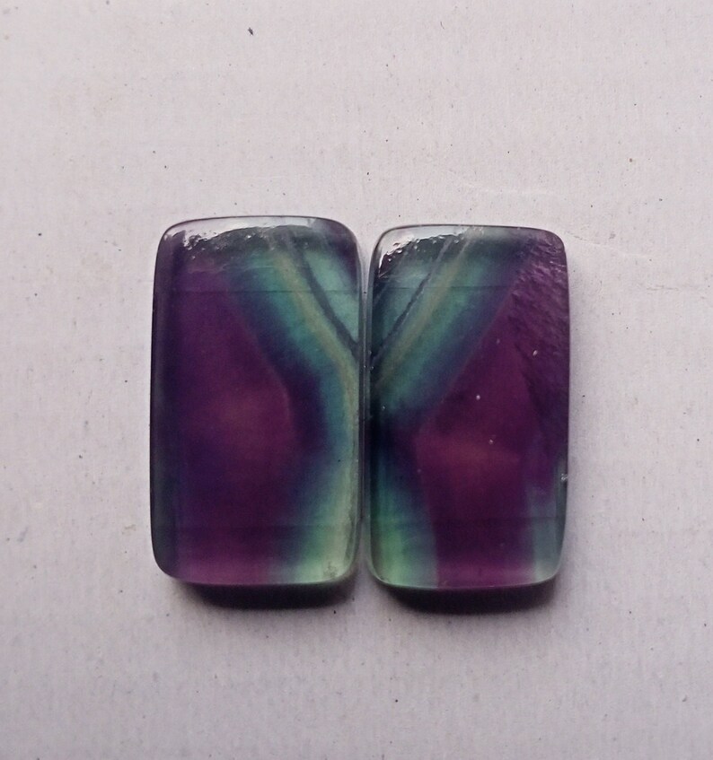Puede incluir: Dos piedras preciosas de fluorita rectangulares con un patr&oacute;n de color morado, verde y blanco.
