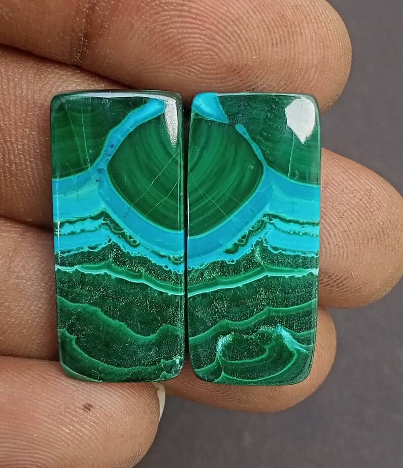 May include: Pair of green and blue malachite cabochons, each with a unique pattern of swirling lines and a smooth, polished surface. These cabochons are ideal for jewelry making or other craft projects.