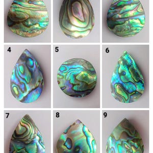 Könnte beinhalten: Neun regenbogenfarbene Abalone-Muschel-Tropfencabochons in verschiedenen Grüntönen, Blau- und Violetttönen. Die Cabochons sind in drei Reihen zu drei angeordnet, wobei jede Reihe von 1 bis 3, von 4 bis 6 und von 7 bis 9 nummeriert ist.