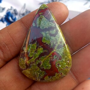K&ouml;nnte beinhalten: Ein tropfenf&ouml;rmiger Cabochon aus gr&uuml;nem, rotem und braunem Jaspis. Der Stein hat ein geflecktes, wirbelndes Muster.