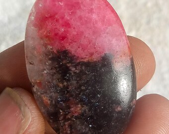 Puede incluir: Una gema ovalada con un llamativo degradado de color. La mitad superior es de un rosa vibrante, que pasa a un negro profundo en la parte inferior. La piedra tiene una superficie pulida, revelando patrones naturales.