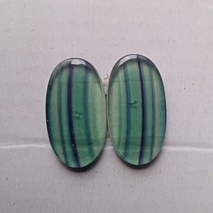 Puede incluir: Dos cabujones ovalados de fluorita verde y azul con estr&iacute;as blancas y moradas.