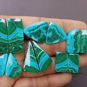 May include: A set of eight cabochon gemstones, cut in various shapes, including rectangular, triangular, and oval. The stones are a vibrant mix of green and blue, with intricate patterns and swirls.